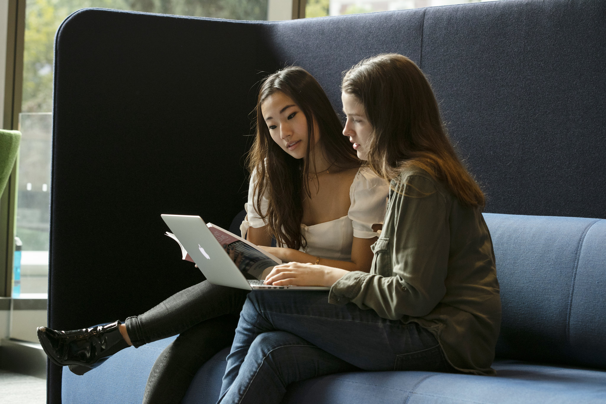 2 female students sit next to each other, using a laptop