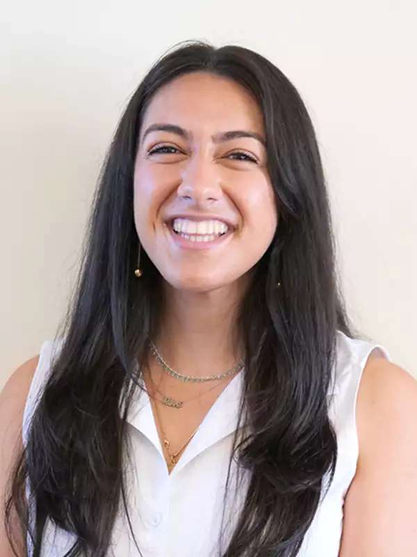 photo of tara smiling wearing a white sleeveless shirt against an off-white background